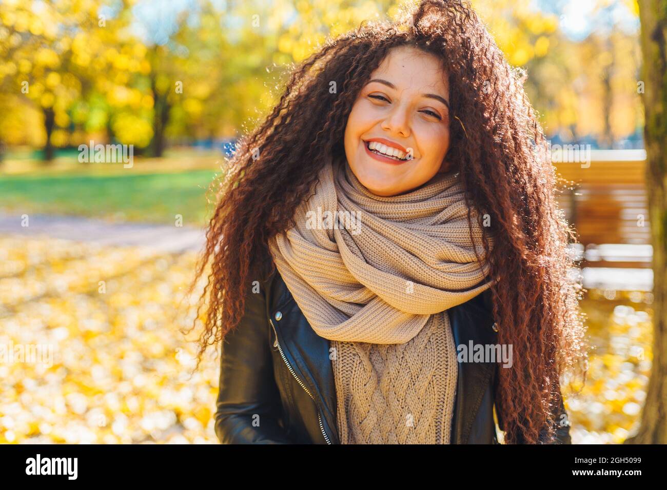 Atractiva mujer de pelo afro con una sonrisa blanca como la nieve con una cálida bufanda Camine en el parque de otoño en un soleado día cálido. Retrato de mujer feliz al aire libre Foto de stock