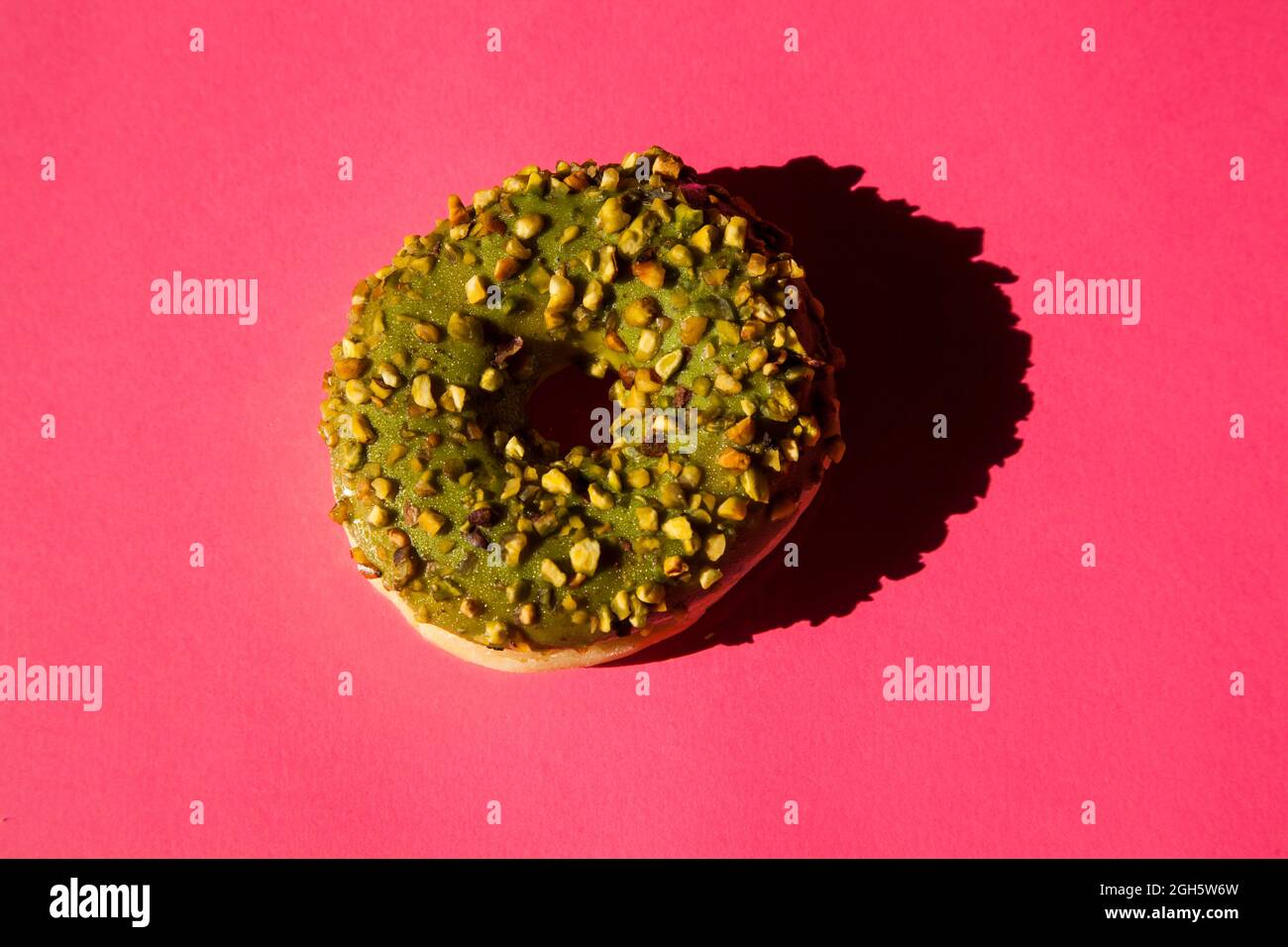 Vista superior de un donuts revestido con un azúcar verde con nueces sobre fondo rosa Foto de stock