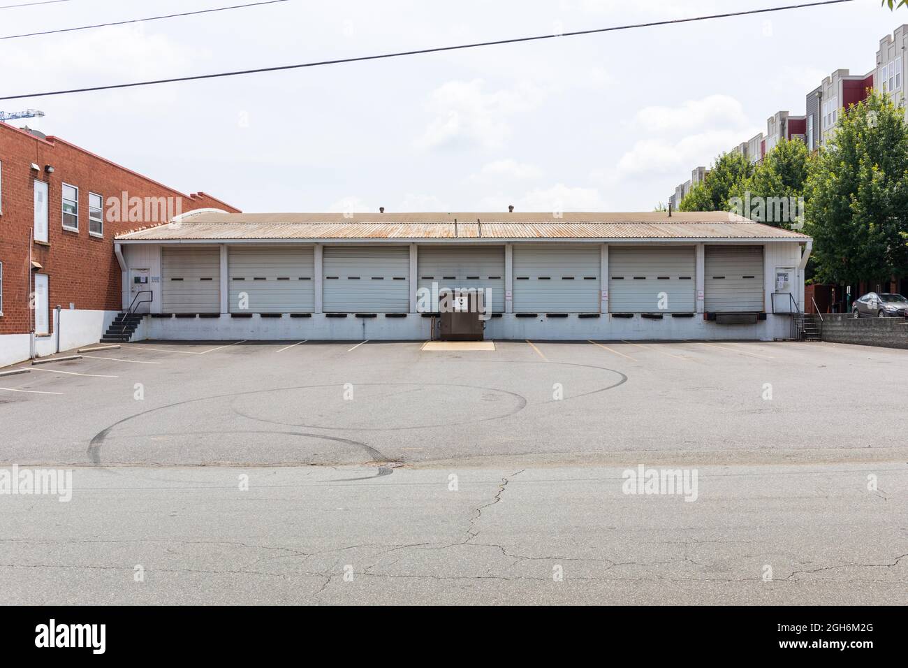 CHARLOTTE, NC, EE.UU.-25 DE JULIO de 2021: Un almacén largo con 7 puertas de bahía, todas cerradas, y un basurero de basura. Aparcamiento vacío. Foto de stock