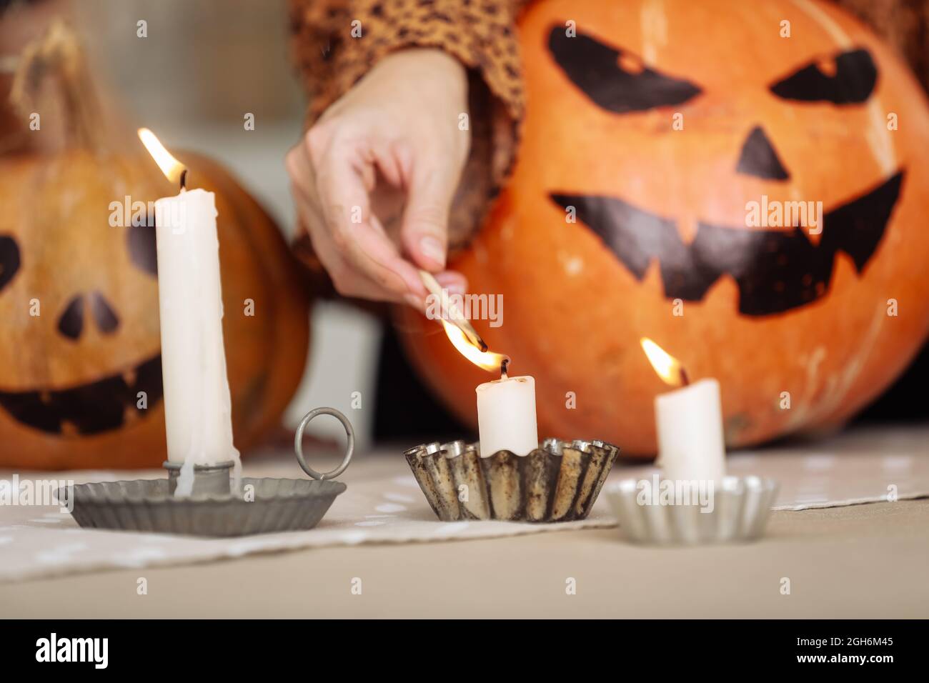 Vacaciones y el concepto del ocio - mano de la mujer con las velas encendidas de los partidos en el hogar en halloween. Calabazas pintadas en un fondo. Tema del horror y hallowe'en Foto de stock