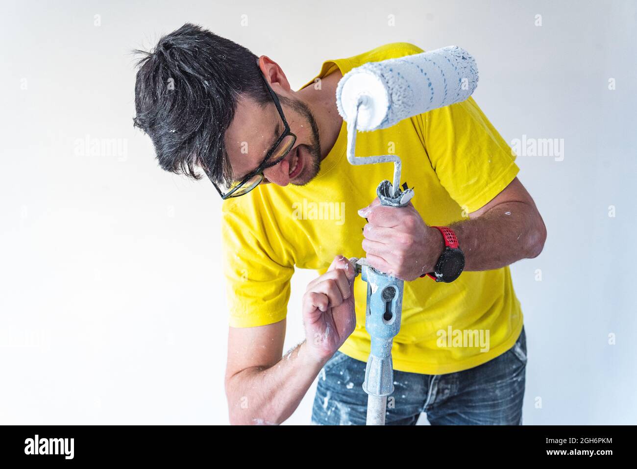 Hombre haciendo fuerza para montar el rodillo de pintura en un palo para pintar el techo. Foto de stock