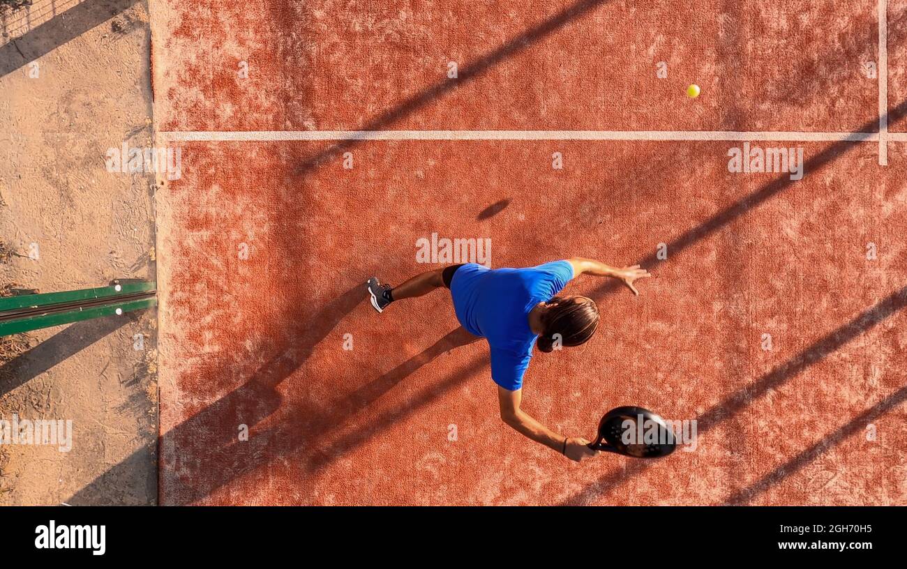 Vista desde arriba de un jugador profesional de pádel que va a golpear el balón con la raqueta en una pista al aire libre. Foto de stock
