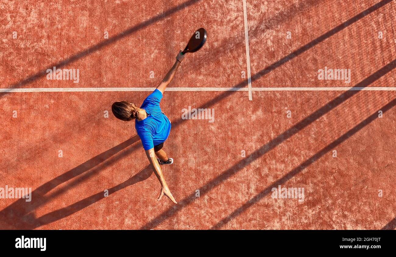 Vista desde arriba de un jugador profesional de pádel que acaba de golpear la pelota con su raqueta en una pista al aire libre. Foto de stock