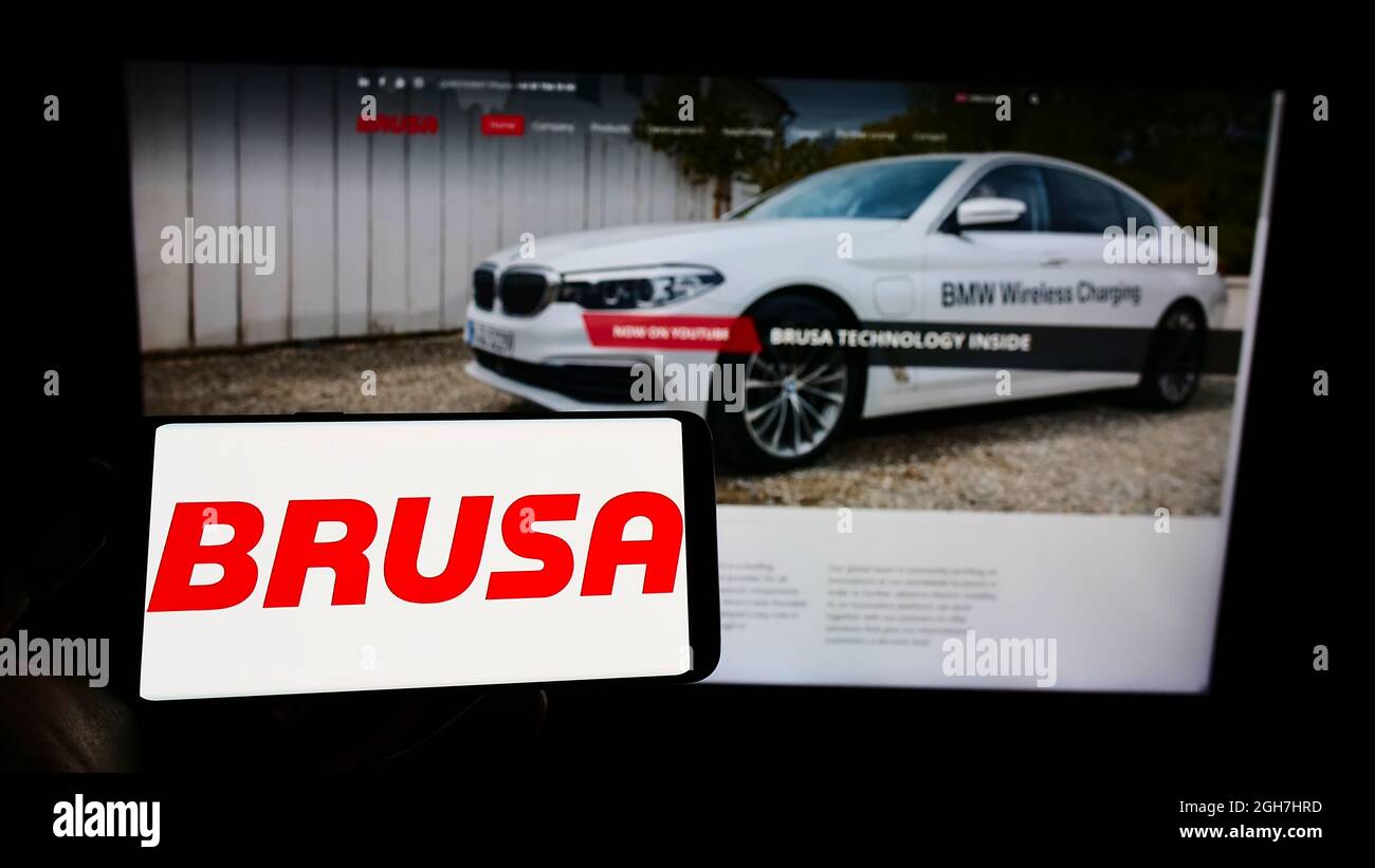 Persona que sostiene un smartphone con el logotipo de la compañía suiza de electrónica BRUSA Elektronik AG en la pantalla frente al sitio web. Enfoque en la pantalla del teléfono. Foto de stock