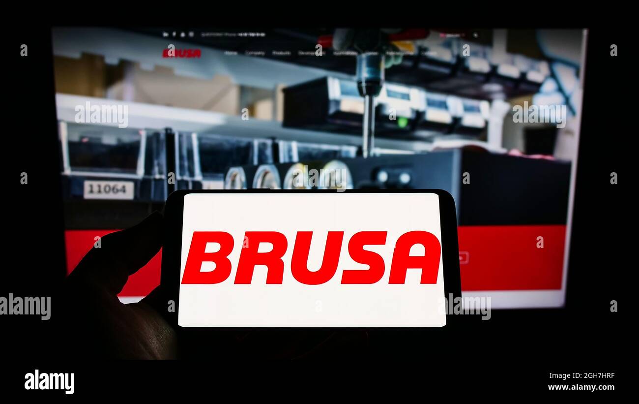 Persona que sostiene el teléfono móvil con el logotipo de la compañía suiza de electrónica BRUSA Elektronik AG en la pantalla frente a la página web de la empresa. Enfoque en la pantalla del teléfono. Foto de stock