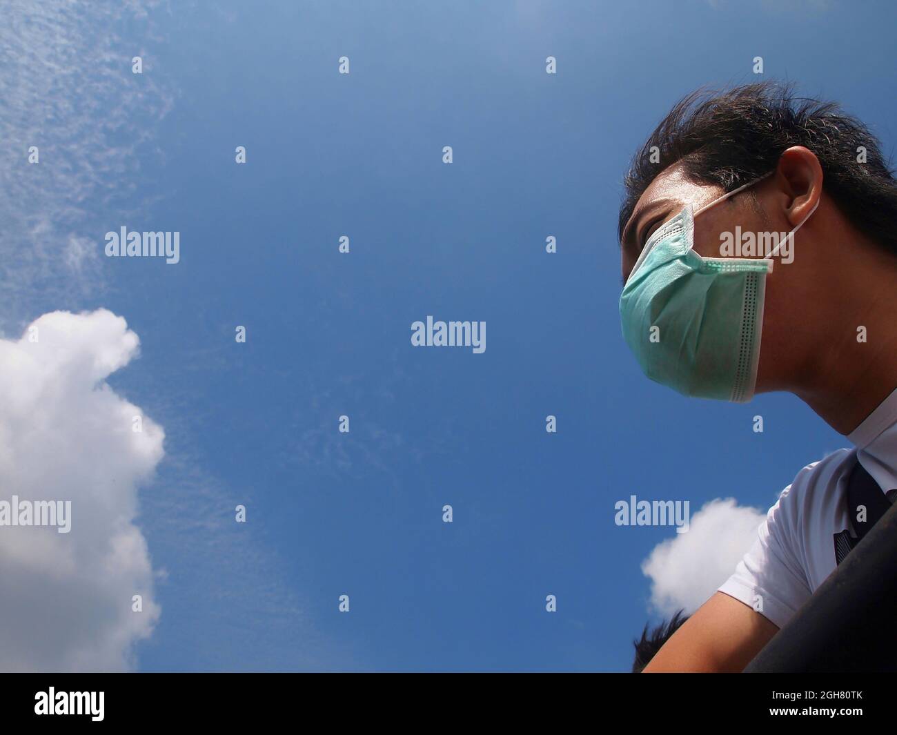 Vista de ángulo bajo hombre asiático con máscara médica. Cielo azul claro. Espacio de copia. Concepto de prevención de enfermedades infecciosas. Foto de stock