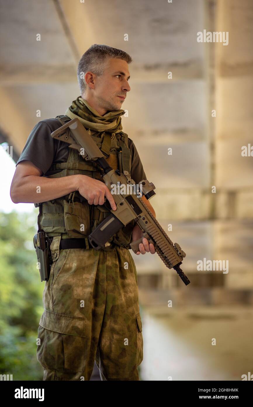 Un hombre de pie con un rifle de asalto airsoft en uniforme militar en  hangar de hormigón Fotografía de stock - Alamy