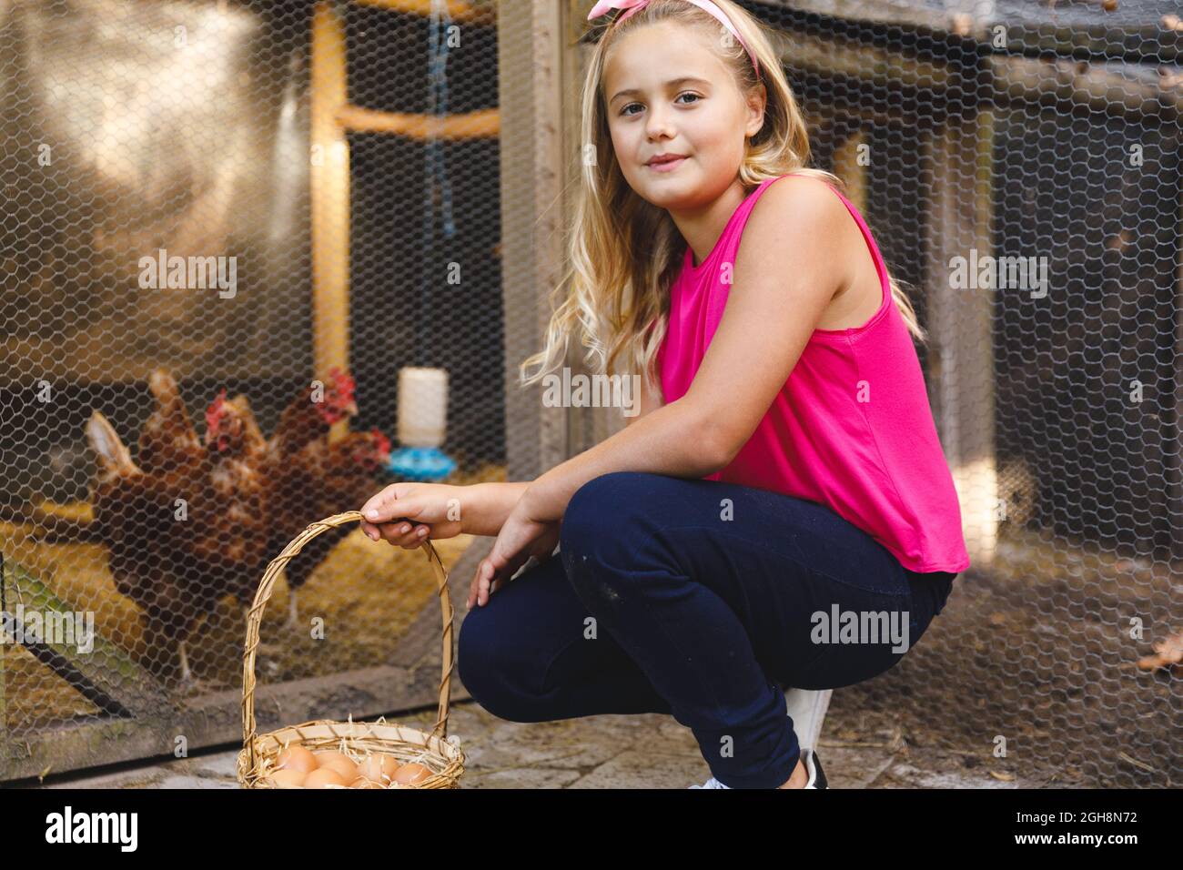 Retrato de sonriente chica caucásica recogiendo huevos de gallina en el jardín Foto de stock