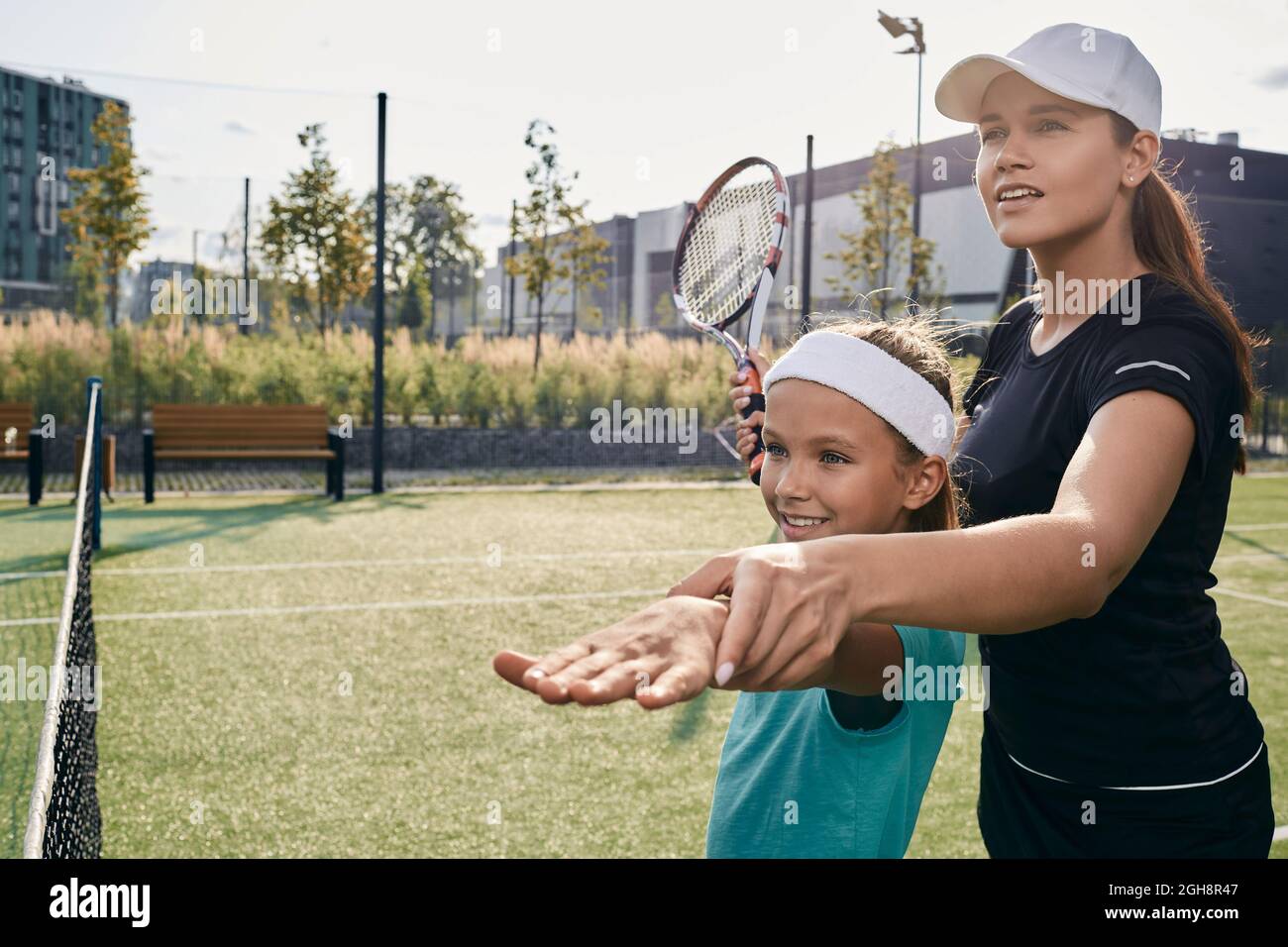 La entrenadora de tenis enseña a la niña a jugar al tenis en la cancha de hierba. Clase de tenis para un niño Foto de stock