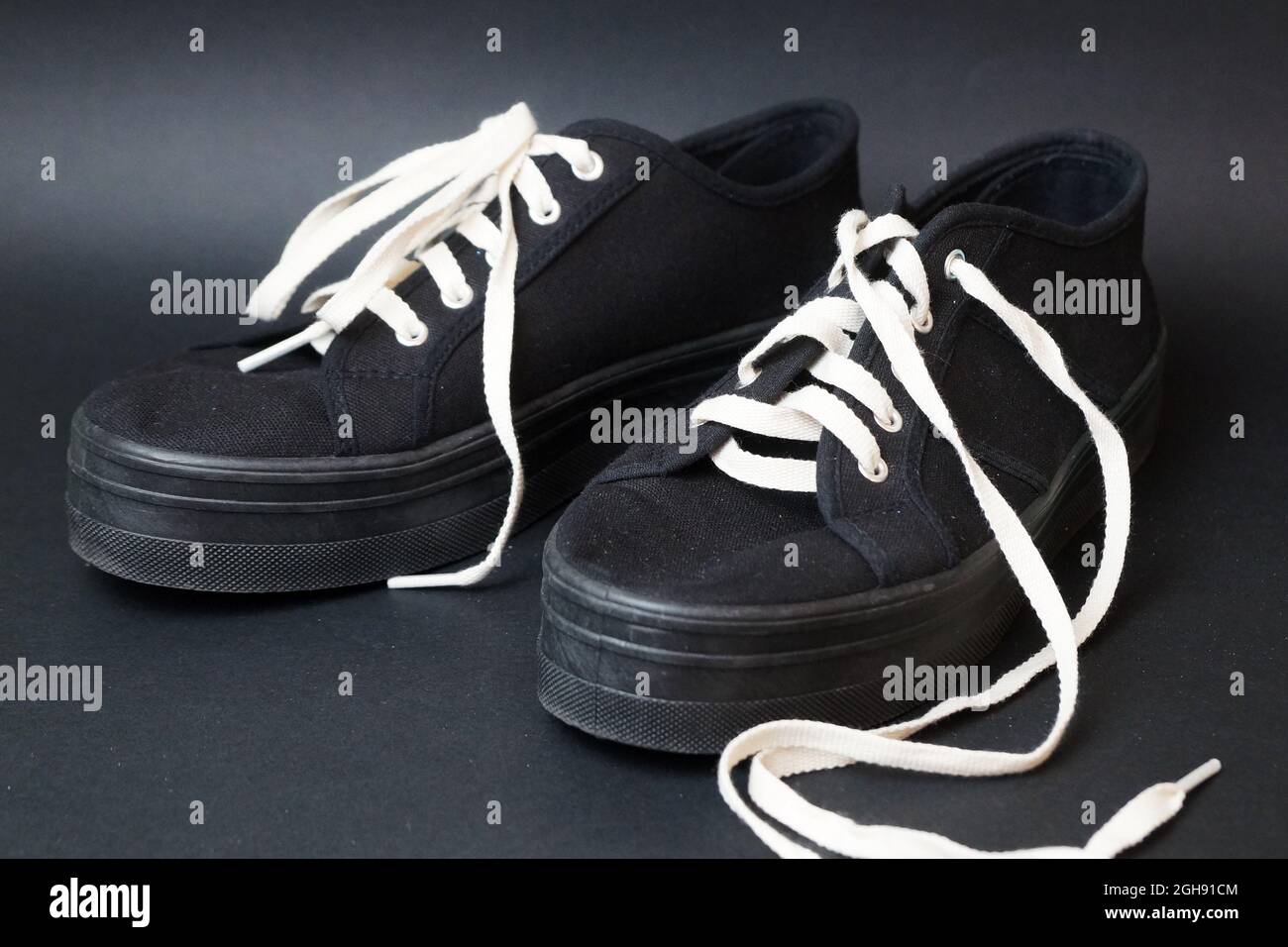 zapatillas de lona negras con cordones blancos desatados sobre un fondo  negro Fotografía de stock - Alamy