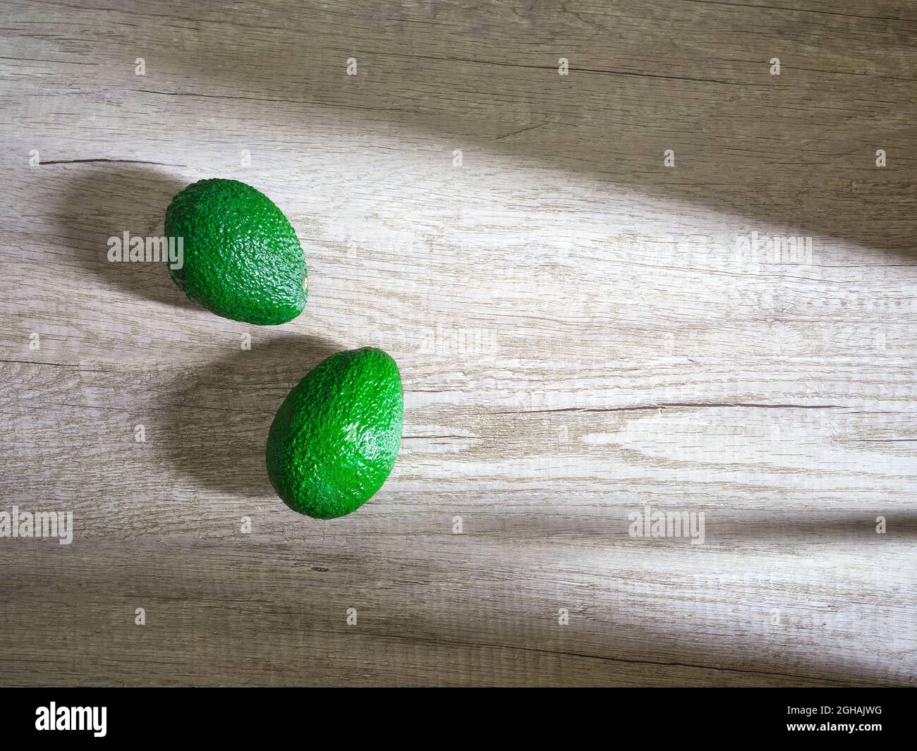 dos aguacates verdes sobre superficie de madera Foto de stock