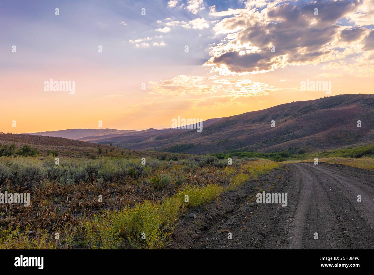 Un camino de tierra que corre a través de un valle hacia la puesta de sol en el noroeste de colorado. Pequeños rayos antiarrugas son visibles en el área superior. Foto de stock