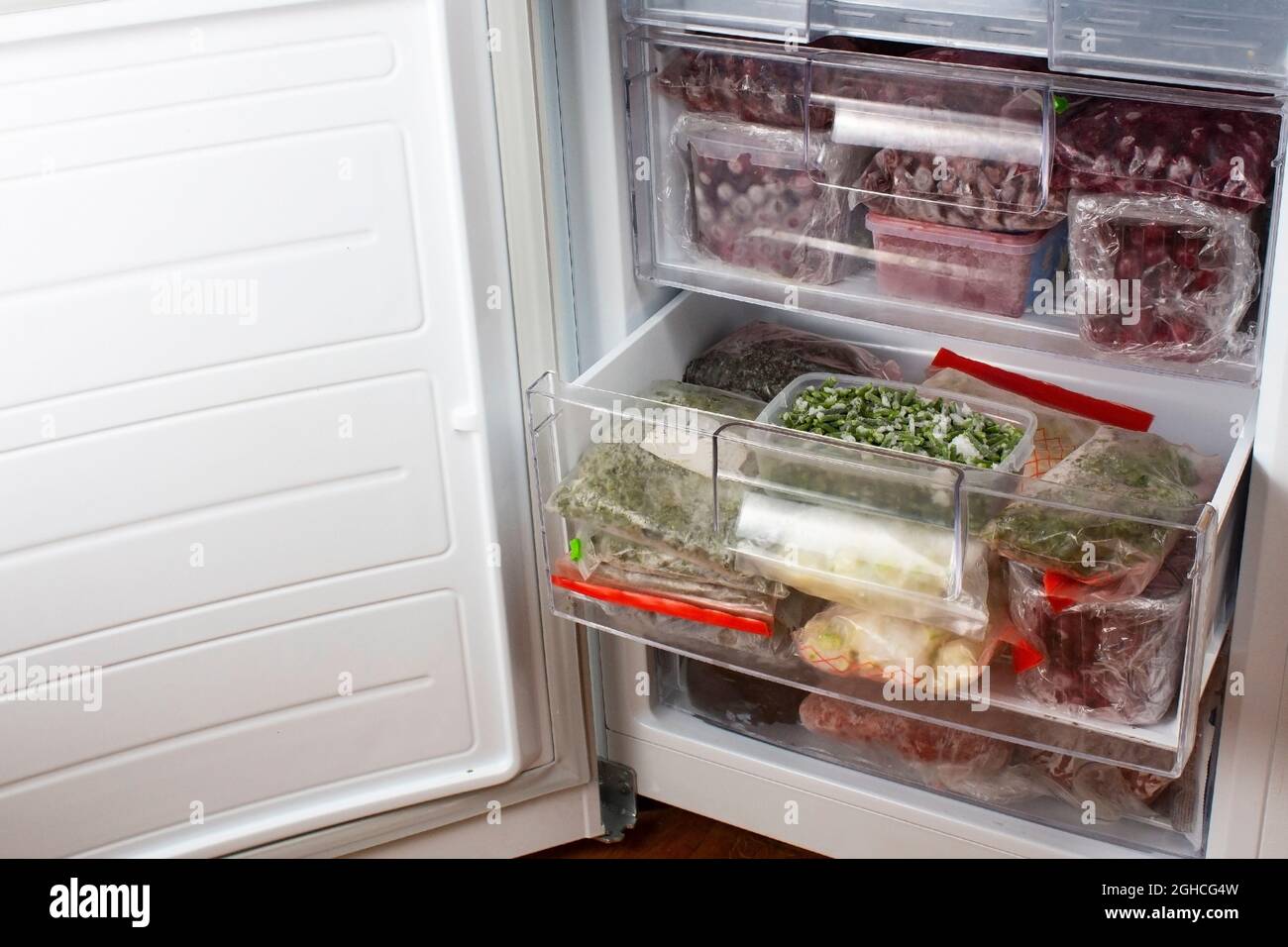 Abra el congelador con cerezas rojas congeladas y verduras congeladas. Almacenamiento de alimentos. Alimentos ultracongelados. Suministros de alimentos para el período de cuarentena. Foto de stock