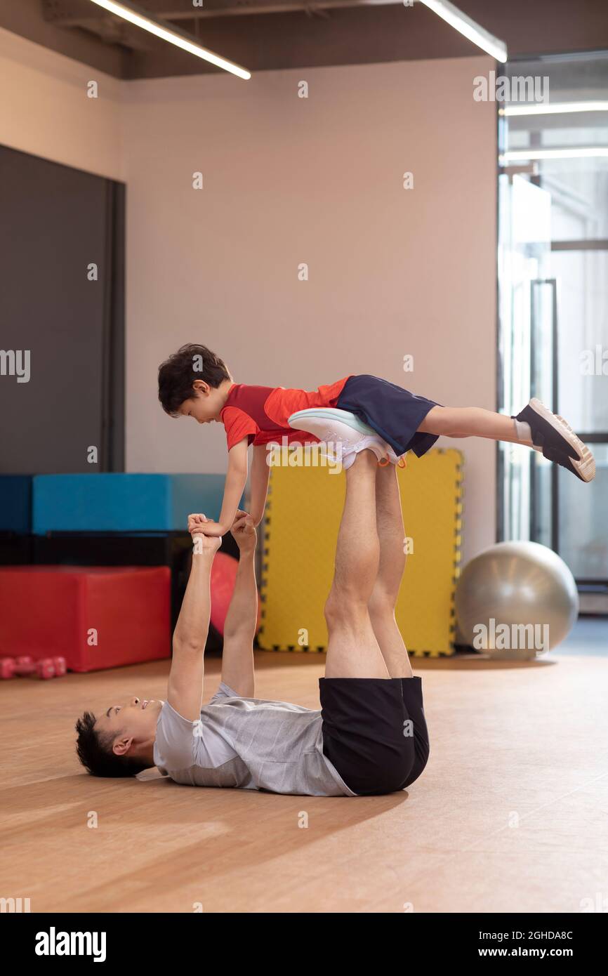 Niño pequeño haciendo ejercicio con su padre en el gimnasio Foto de stock