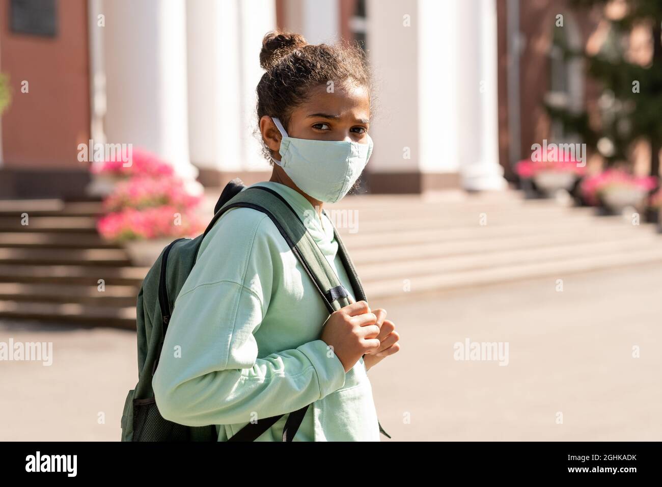 Una linda colegiala de raza mixta con ropa de sport y máscara protectora que va a la escuela por la mañana Foto de stock