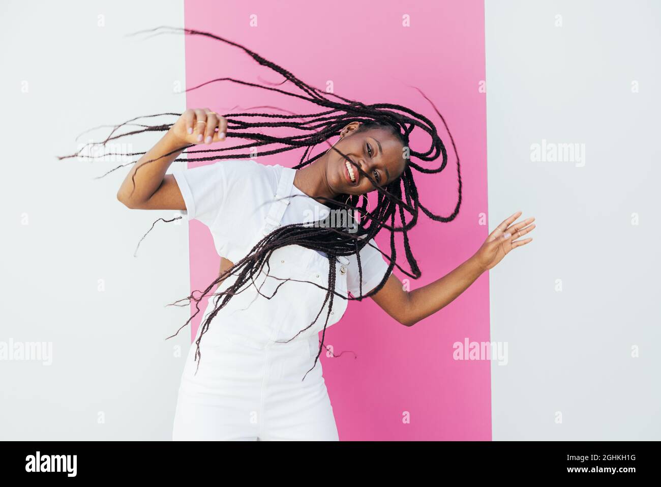 Joven mujer feliz con el pelo largo que se divierte contra la pared blanca con la raya rosada Foto de stock