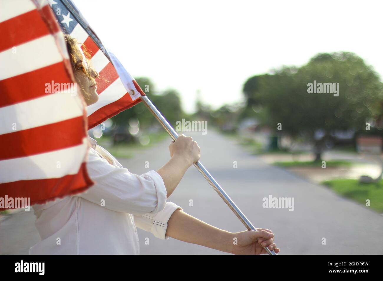Joven pelirroja hispana y caucásica con gafas de sol que ondean la bandera americana afuera. Foto de stock