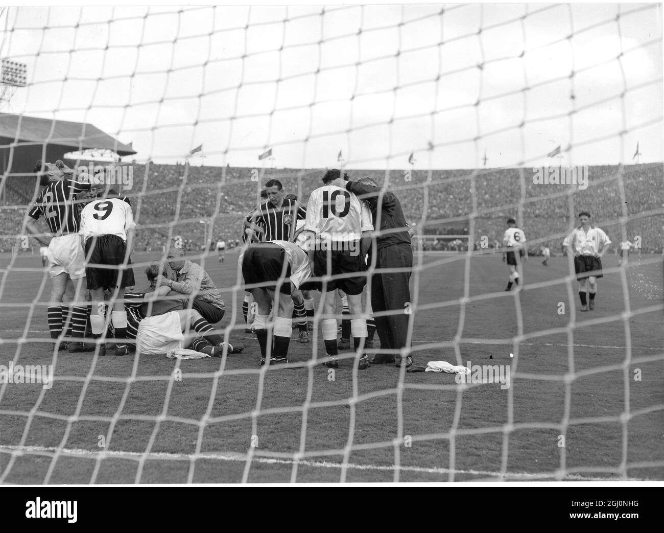 El portero de Manchester City Bert Trautmann (c) recibe tratamiento del entrenador de la ciudad después de romper su cuello buceando a los pies de Peter Murphy de Birmingham City (9) Foto de stock