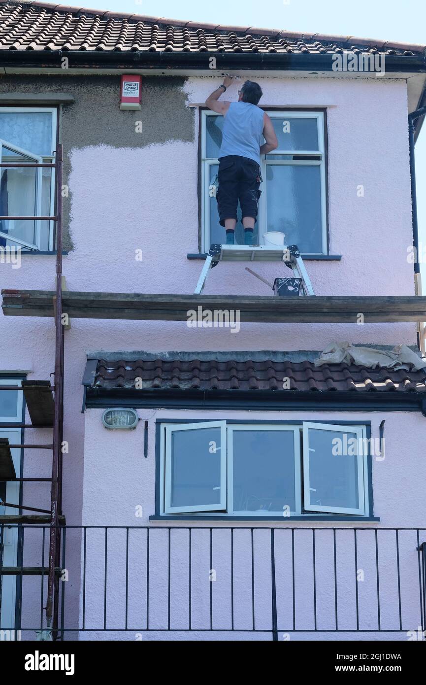 Pintar una casa con equipo improvisado para llegar a una zona difícil en una casa de 1930s. Foto de stock