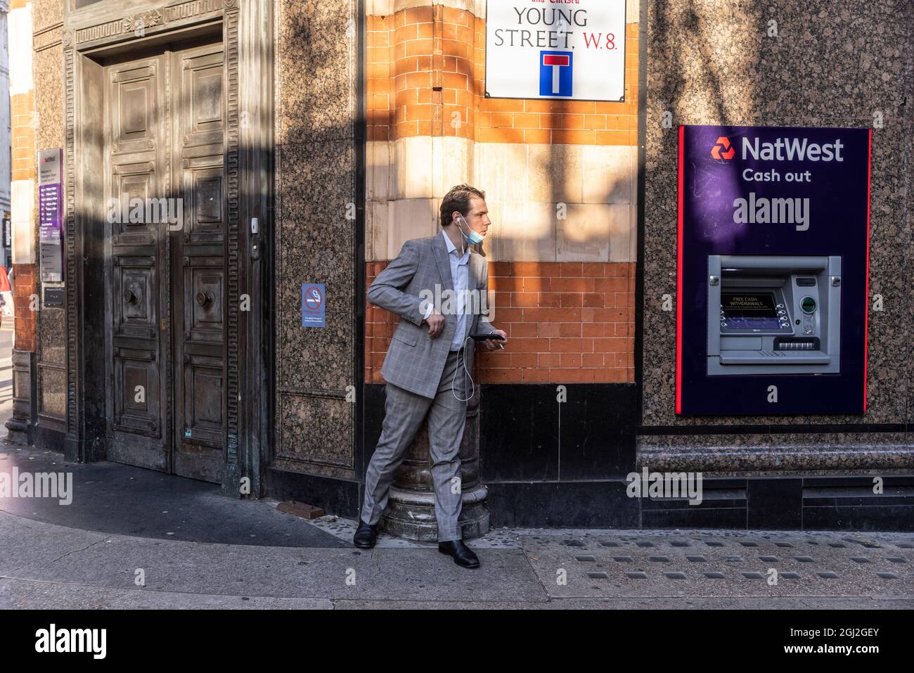 Hombre de negocios acechando detrás de la esquina de una pared en Young Street, Kensington, Central London, Reino Unido Foto de stock