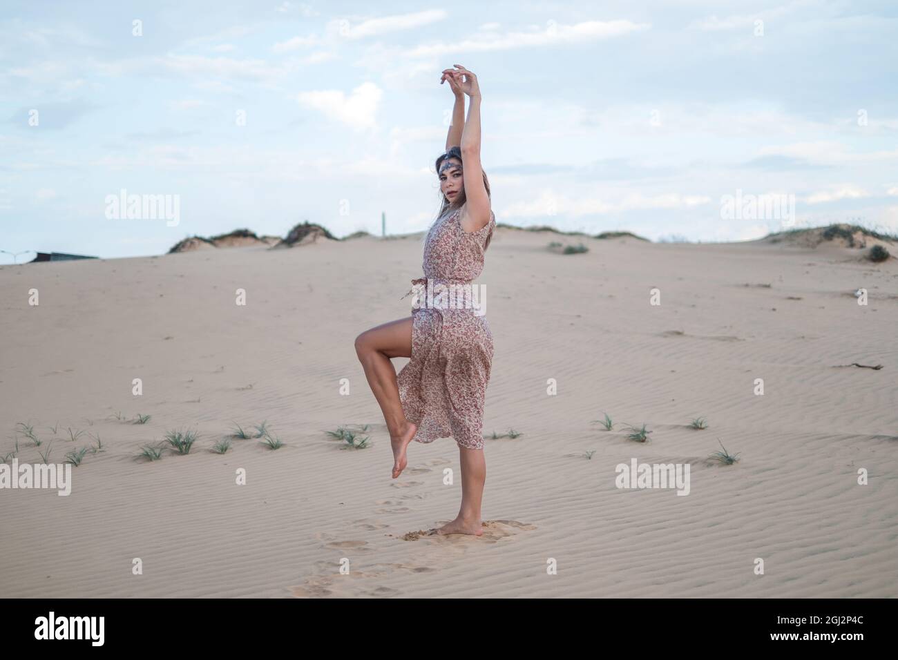 Vista pintoresca de la hermosa mujer rubia en vestido largo casual caminando y bailando en el desierto en día soleado durante las vacaciones de verano. Dunas de arena. Foto de stock