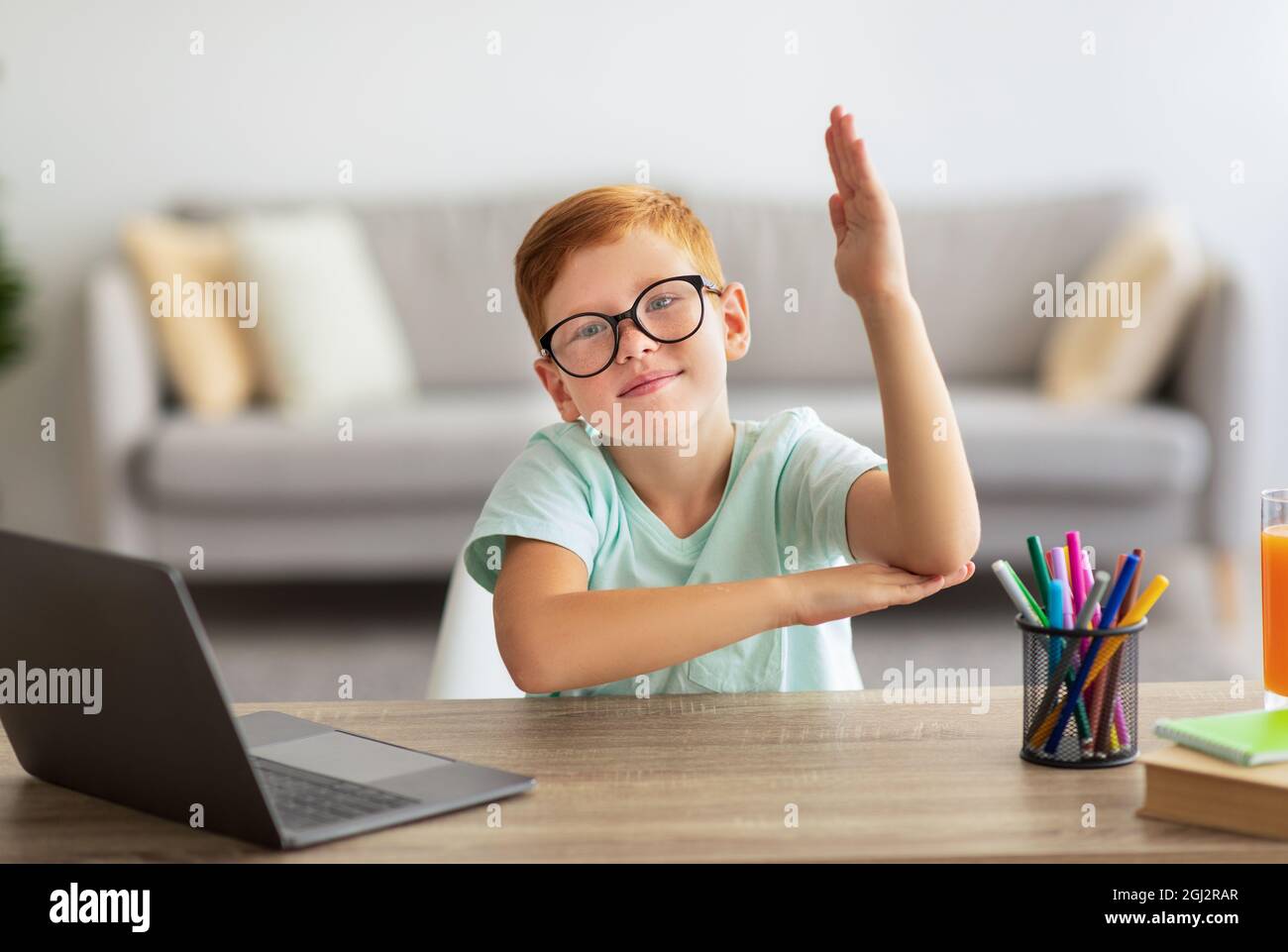 Lindo niño redheal escuela levantar la mano mientras que tiene clase en  línea, permanecer en casa durante el cierre COVID-19, niño sentado en el  escritorio con ordenador portátil y statio Fotografía de