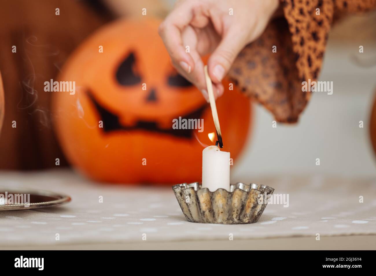 Vacaciones y el concepto del ocio - mano de la mujer con las velas encendidas del fósforos en el hogar en halloween. Calabazas pintadas en un fondo. Tema del horror y Hal Foto de stock