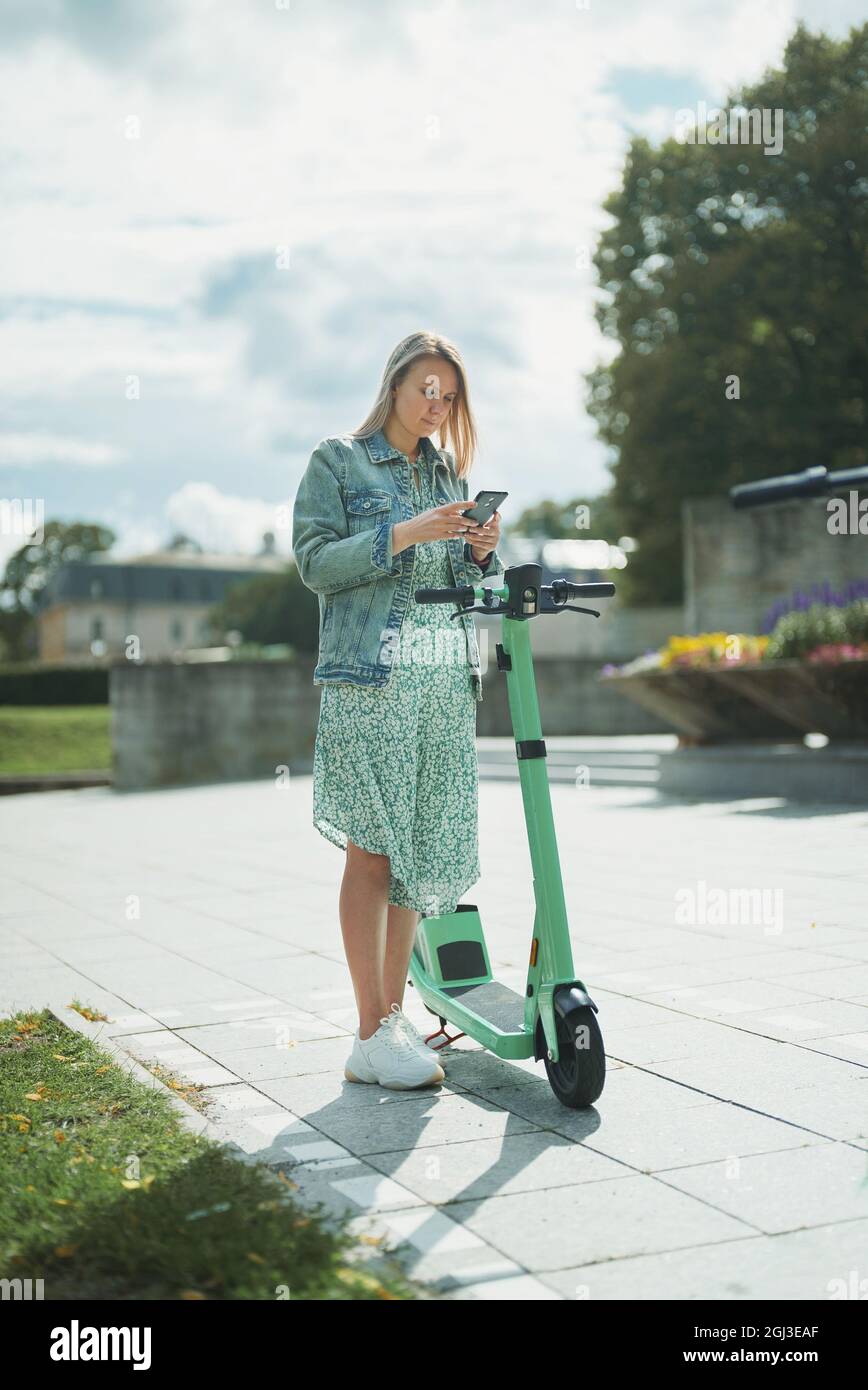 Mujer que utiliza la aplicación en el smartphone para desbloquear el scooter eléctrico en la calle. Foto de stock