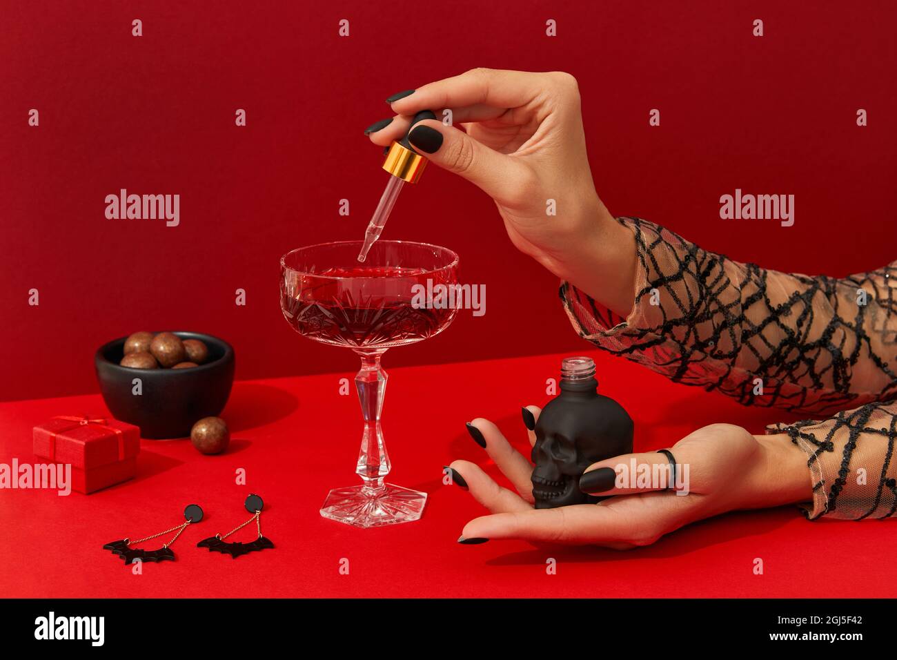 Las manos de las mujeres con un diseño de uñas espeluznante cocer un cóctel de halloween de arándanos en una mesa roja Foto de stock