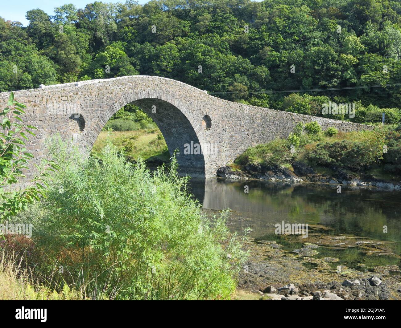 El puente Clachan, de arco sencillo y con respaldo de joroba, se conoce como el puente sobre el Atlántico, que conecta el continente escocés con la isla de Seil. Foto de stock