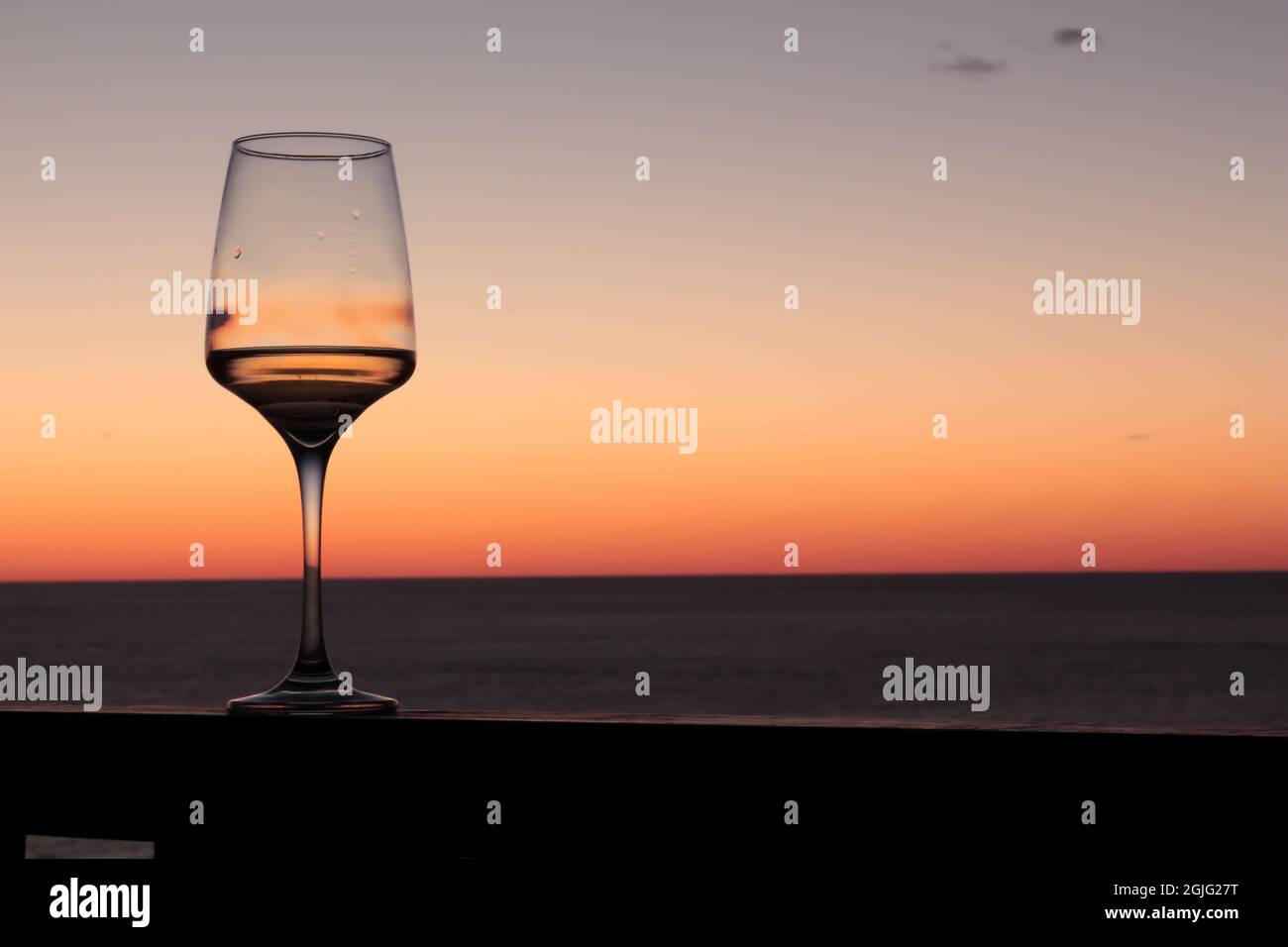 Copa de vino blanco con puesta de sol en el océano en el fondo. Foto de stock