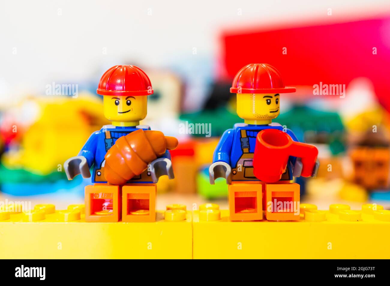 POZNAN, POLONIA - 09 de septiembre de 2021: Los trabajadores de la  construcción de juguetes LEGO con casco de seguridad que tienen un descanso  sentado en bloques comiendo un cruasán y bebiendo