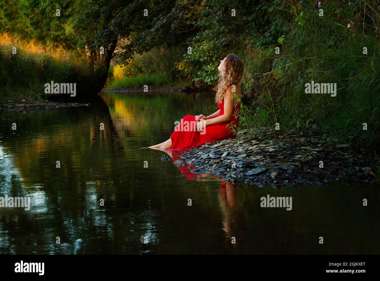 Una hermosa chica con un vestido rojo junto a un río Foto de stock