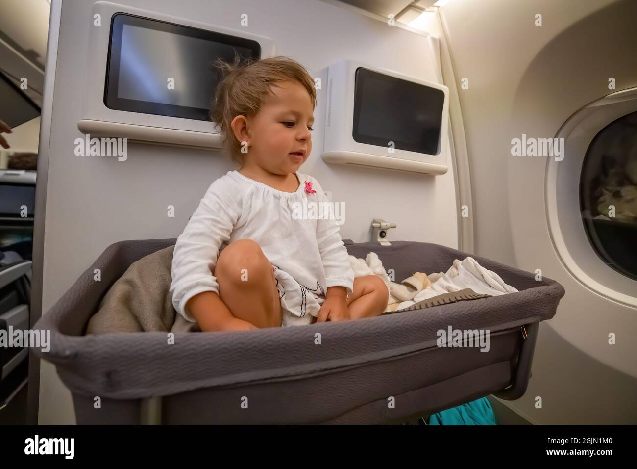 lindo asiento de bebé niña en una cuna especial en el avión. Un bebé mira  al lado en la cuna en el avión. Vuelo firme. Un bebé a bordo Fotografía de  stock -