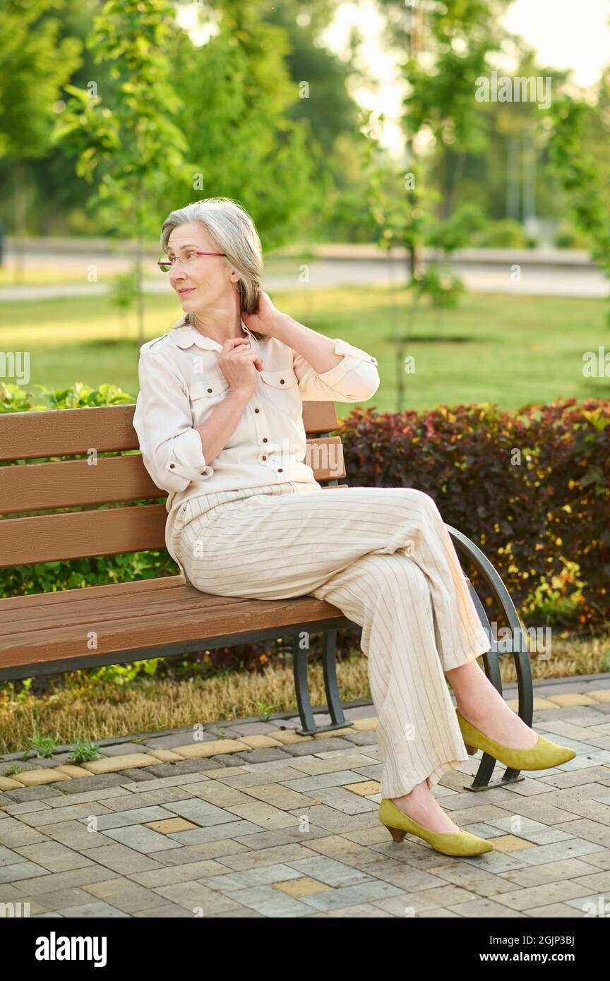 Mujer con gafas sentada en el banco del parque Foto de stock