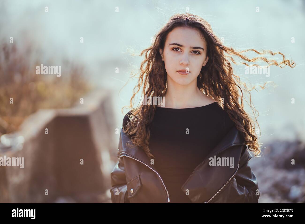 Retrato al aire libre de una hermosa niña adolescente morena en la chaqueta de cuero negro con humo en el fondo Foto de stock
