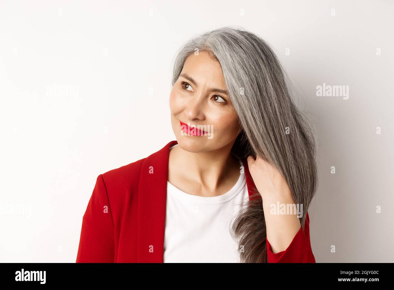 Concepto de belleza y cuidado del cabello. Primer plano de la elegante mujer  asiática mayor mostrando un cabello gris brillante y saludable, sonriendo y  mirando a un lado, fondo blanco Fotografía de