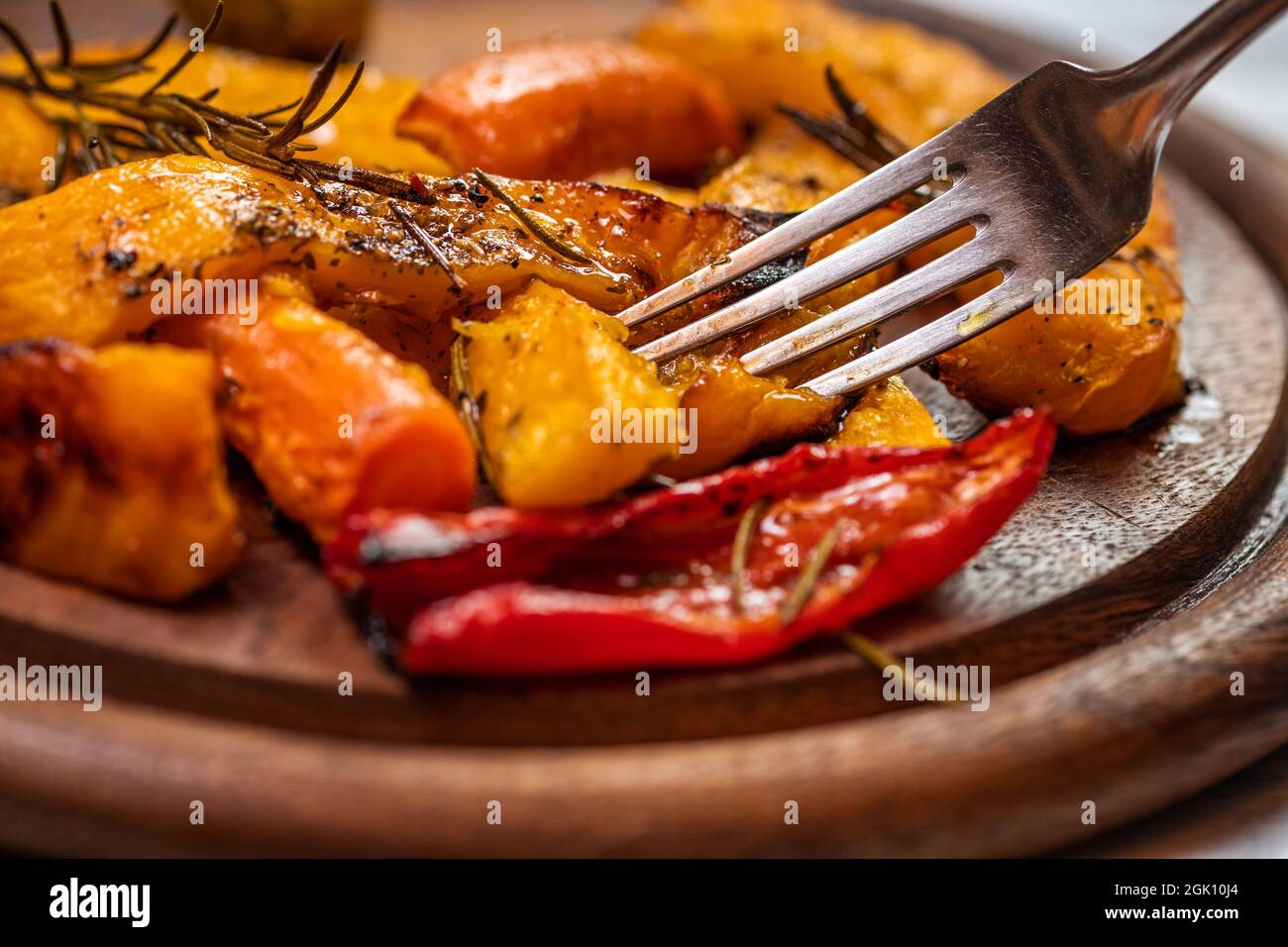 Comer calabaza y verduras a la parrilla. Primer plano tenedor en comida asada en plato de madera Foto de stock