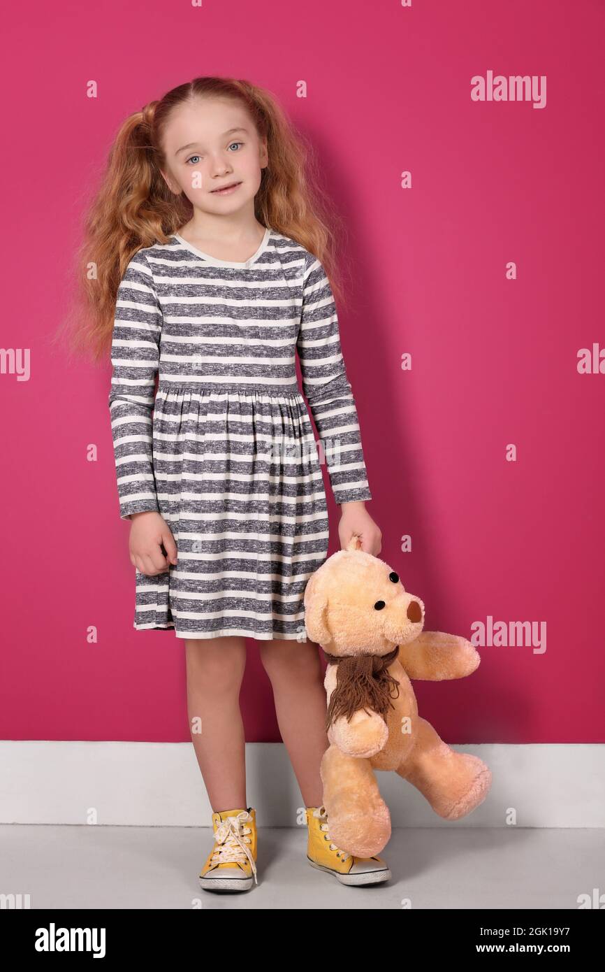 Niña pequeña en vestido a rayas sosteniendo osito de peluche cerca de la  pared rosa Fotografía de stock - Alamy