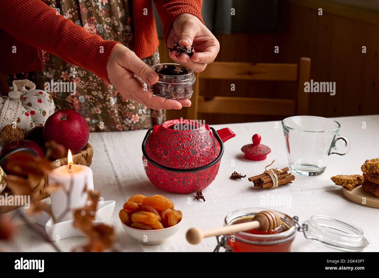 Acogedores días de otoño. Mujer con suéter naranja, prepara té con tetera roja sobre la mesa con manteles de lino. Estado de ánimo aromático. Vibraciones de otoño. Té bebiendo.Than Foto de stock