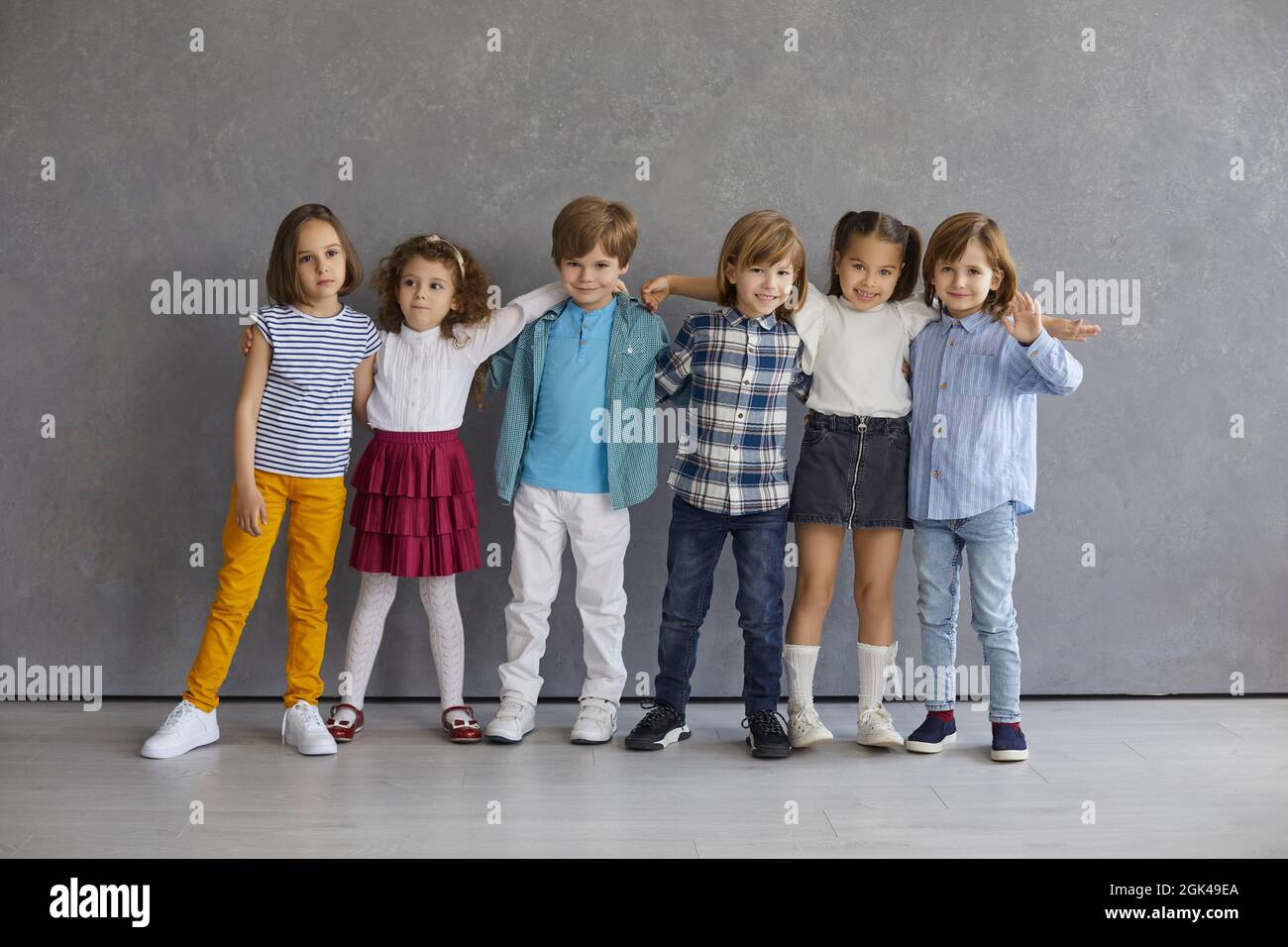 Retrato niños pequeños divertidos de pie en fila abrazando contra el telón de fondo de una pared gris Fotografía de stock Alamy