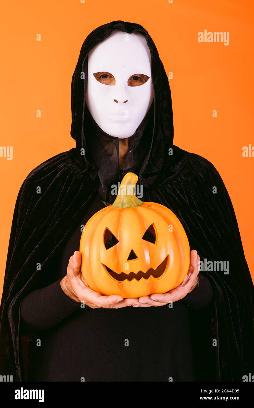 Cintura su sector Retrato de una persona con máscara blanca de Halloween asesino, capa y  capucha, sosteniendo una calabaza jack-o'-linterna, vestido para Halloween  sobre fondo naranja Fotografía de stock - Alamy