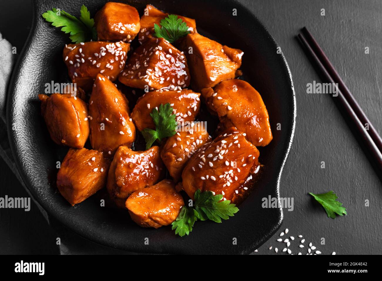 Trozos de pollo teriyaki con sésamo y verduras sobre fondo negro de cerca. Comida de estilo asiático: Filete de pollo asado con salsa teriyaki. Foto de stock