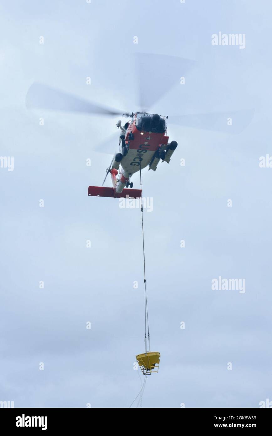 Se muestra un helicóptero MH-60 Jayhawk, del sector de la Guardia Costera de EE.UU. Columbia River, izado de un contenedor lleno de hormigón mientras se realiza el entrenamiento de vertido de hormigón con SIDA para el equipo de navegación Astoria, miércoles, 18 de agosto de 2021, en Astoria, Oregón. Ambas tripulaciones llevaron a cabo el entrenamiento de vertido de hormigón para prepararse para un proyecto de reconstrucción que se avecina, donde se verterán una base para nuevas ayudas a la navegación. Foto de stock