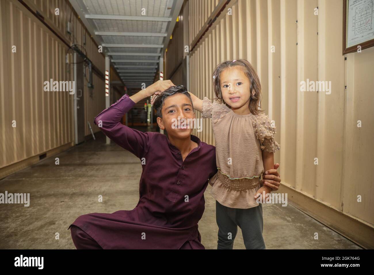 Un niño afgano sonríe con su hermana en un alojamiento para evacuados en el CENTCOM AOR, 21 de agosto de 2021. Los evacuados calificados recibirán apoyo, como alojamiento temporal, alimentos, exámenes médicos y tratamiento. Foto de stock