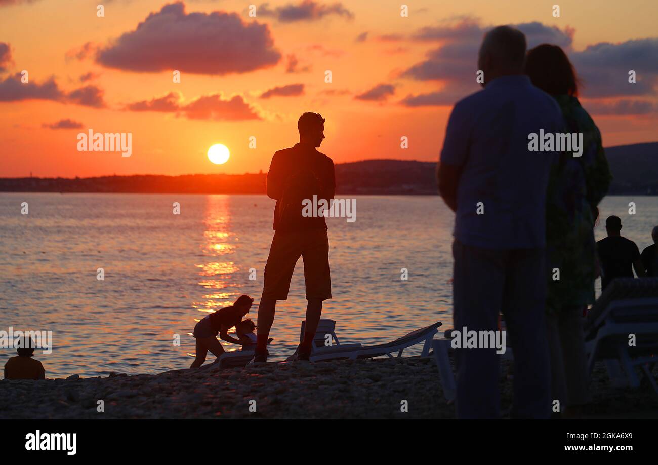 Hermosa foto de una puesta de sol en el mar con turistas de vacaciones en la playa Foto de stock