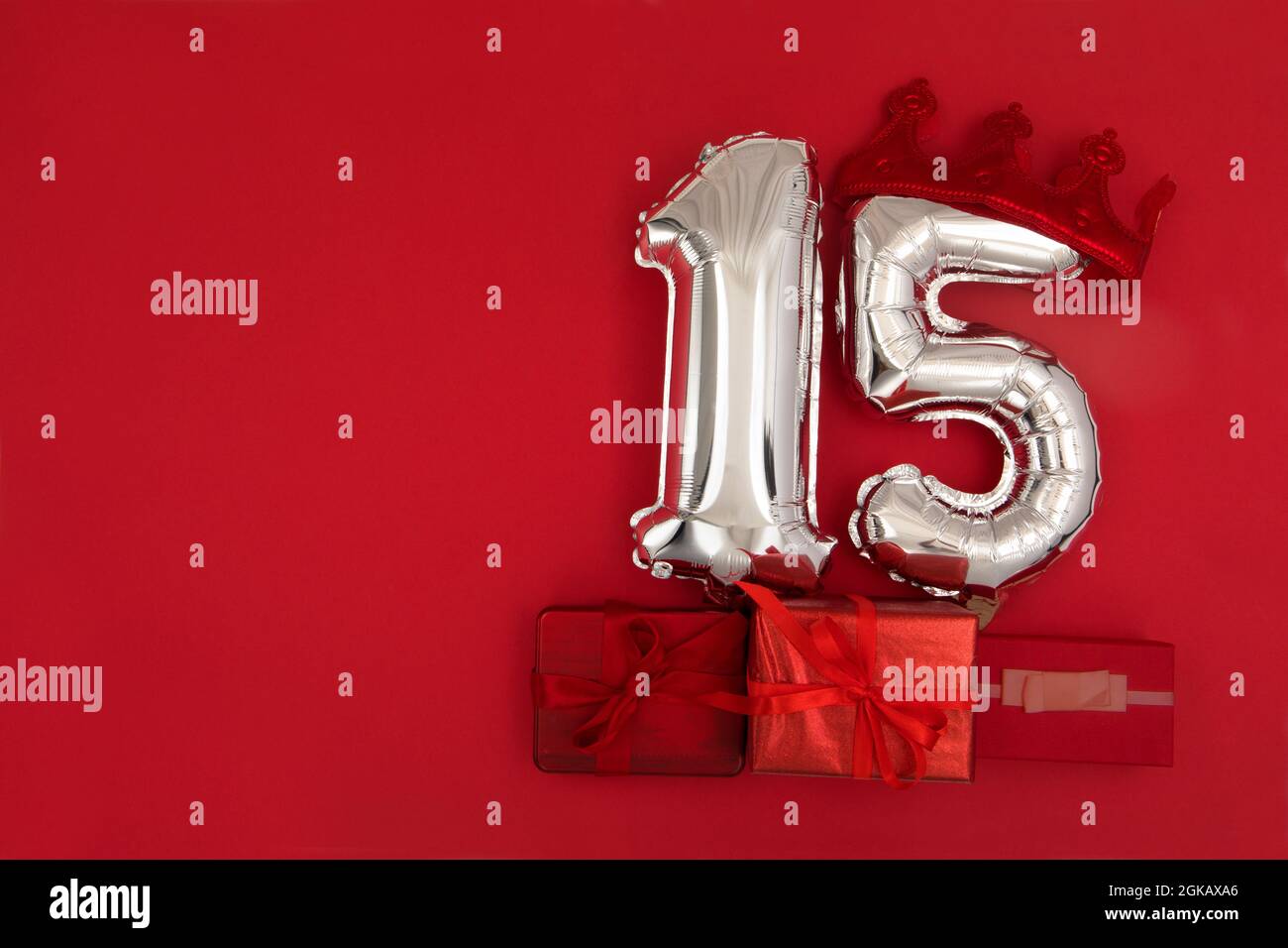 Globos de aire plateados en aluminio que muestran el número 15 quince puestos sobre fondo rojo con regalos envueltos para el concepto de aniversario de cumpleaños Foto de stock
