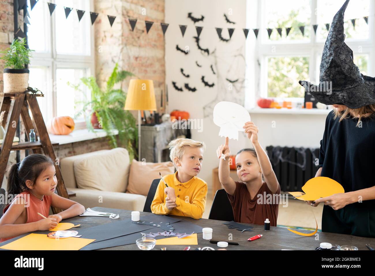 Pequeña niña apuntando al símbolo de papel de halloween mientras se muestra a lindo niño a la mesa Foto de stock