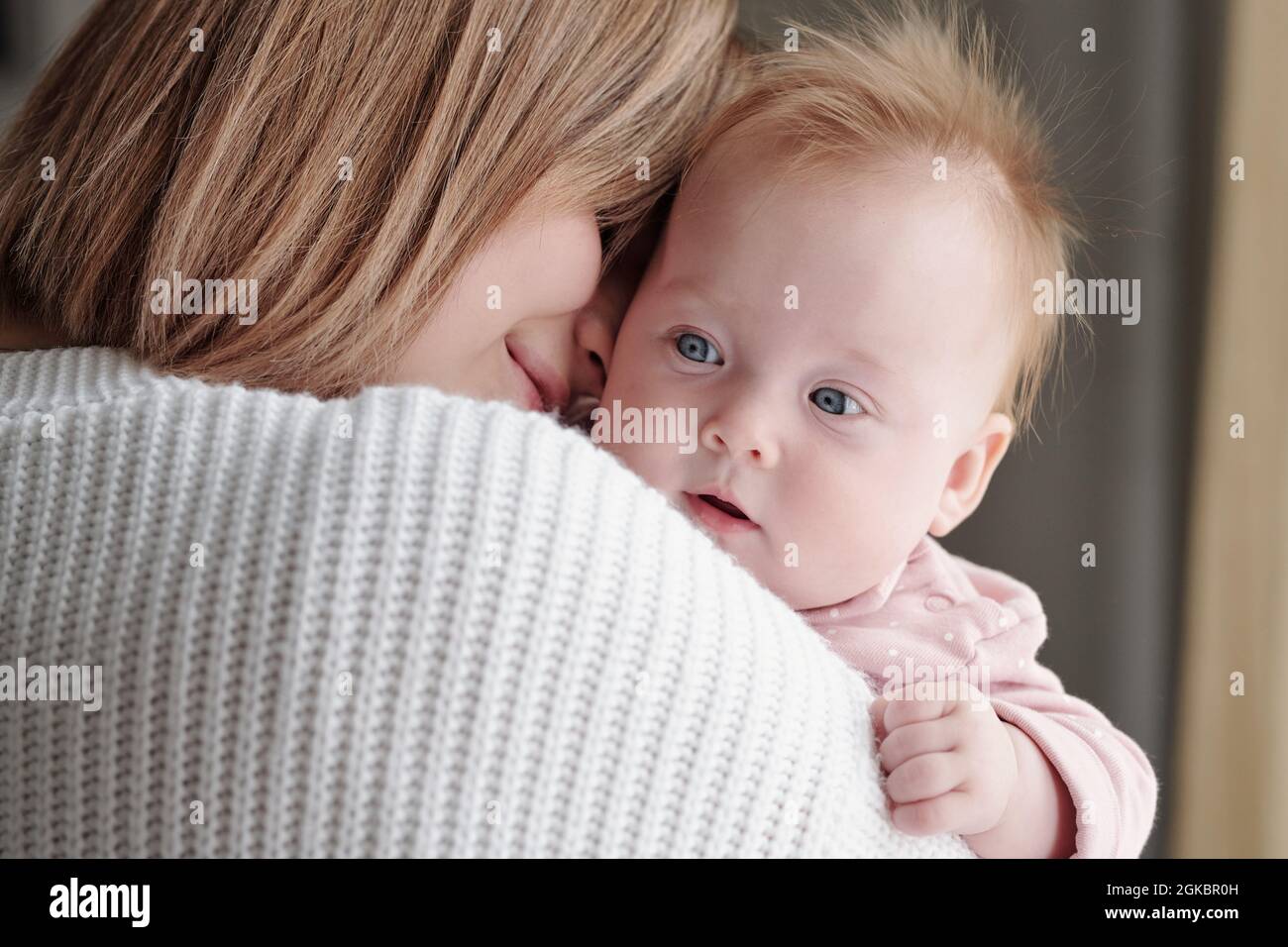 Cara de adorable niña en manos de su feliz joven madre afectuosa Foto de stock