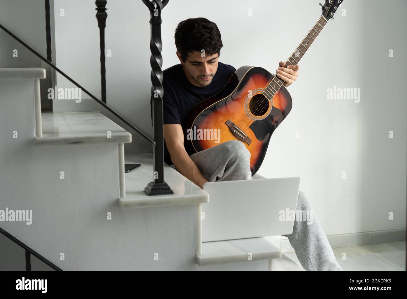 Hombre joven con guitarra acústica sentado en las escaleras y viendo video  tutorial en el portátil mientras aprende a tocar instrumentos musicales  durante el tiempo libre Fotografía de stock - Alamy